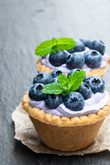 Mini tarts with blue cream and fresh blueberries on black stone background