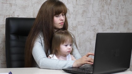 Working mother with her little daughter at table. Busy woman working on laptop with baby on hands. Working mom with beautiful infant on hands in cozy home. Female freelance work. Modern motherhood