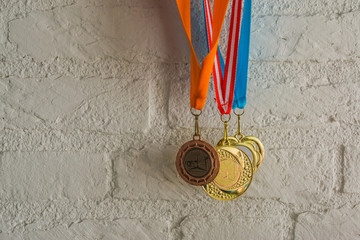 rhythmic gymnastics medals hanging in front of a white brick wall, sport achievements
