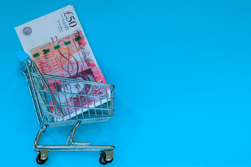 Small toy pushcart with 50 pounds banknote inside on a blue background