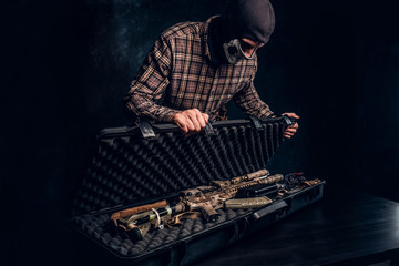 Illegal sale of weapons, black market, the criminal opens the case with an assault rifle and shows it to the buyer. Studio photo against a dark textured wall