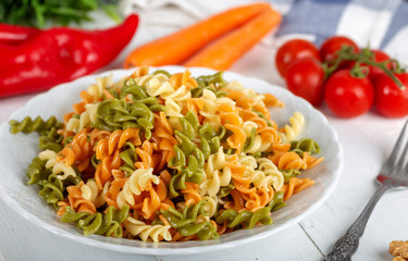 Multicolored pasta with vegetable on wooden background ve vegetables
