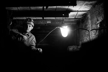 A young guy in a protective suit and helmet sits in a tunnel with a burning scrapbook. Miner in mine