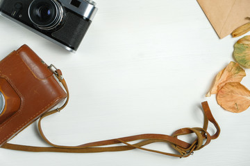 Vintage camera with leather case and dried leaves with craft paper envelope on a wooden white background.