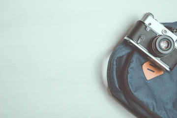 Retro camera lies on a fashionable backpack on a white wooden background.