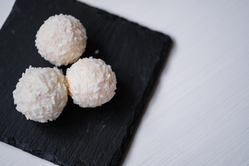 White coconut candy balls in plate shale dishes on rustic wooden background.