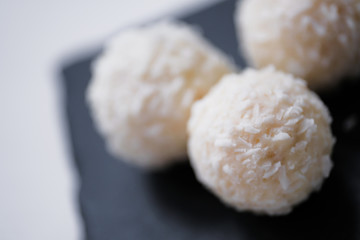 White coconut candy balls in plate shale dishes on rustic wooden background.