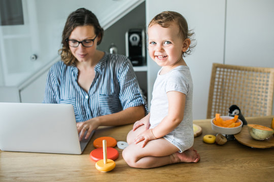 Mother working on laptop and toddler sitting on table