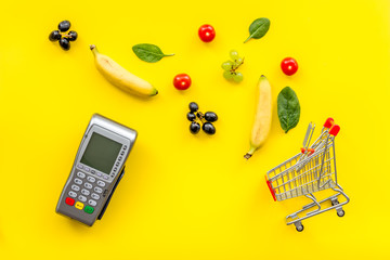 Online shopping concept with trolley, card machine near producs on yellow background top view