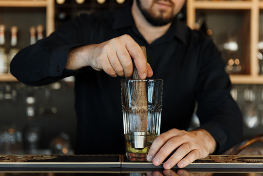 Crop man smashing fruit in cocktail glass
