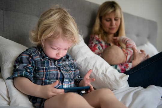 Mother breastfeeding baby while toddler son uses phone