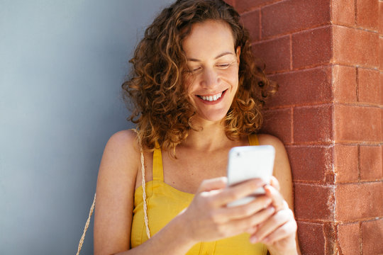 Woman wearing yellow dress using her phone on the street.