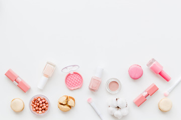 Make-up artist desk with powder, nail polish, decorative cosmetics and macaroon cookies white background top view mokeup