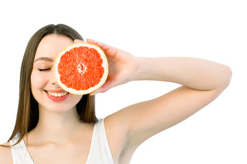 Portrait of young beautiful woman with healthy perfect skin holds piece of grapefruit, closing one eye. Skincare, facial treatment, cosmetology concept. Copy space. Isolated on a white background