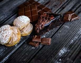 Gourmet slice of brownie, two sandwich cakes and peaces of chocolate on the black table.