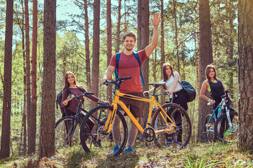 Group of young friends hiking through the forest with bikes on a beautiful summer day