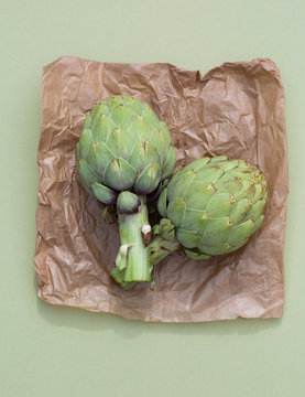 Two globe artichokes on brown paper and green background