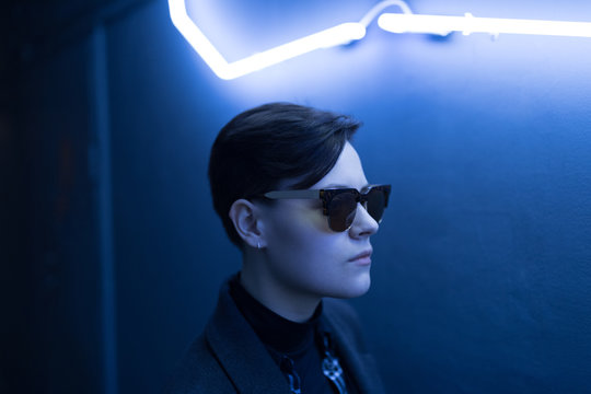 Portrait of short-haired woman with sunglasses under neon light