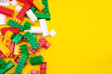 Colorful plastic construction blocks frame on yellow, copy space for your text. Educational children toys on bright yellow background top view.