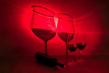 Glasses of red wine cast shadow on gray background with red light