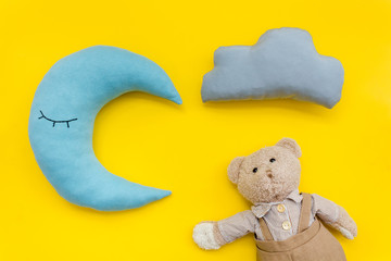 Baby care concept with moon pillow, clouds, teddy bear and toy for sleep of newborn on yellow background top view