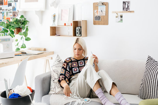 Young woman knitting on sofa