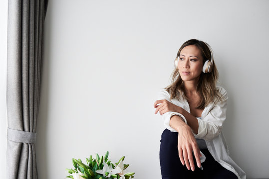 Asian woman thoughtful listening music in headphones.