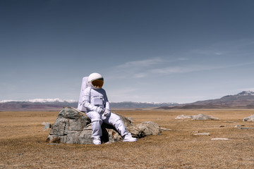 Person in cosmonaut costume sitting on rock