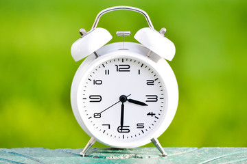 White alarm clock on green background. 