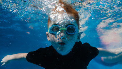 A young boy in a wetsuit blows air bubbles underwater
