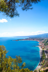 Fototapeta na wymiar Blue Ionian sea near Taormina luxury resorts coastline, bright sunny summer day. Beautiful tree frame. Sicily island, Italy. 