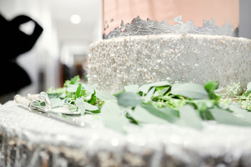 the bottom of the beautiful silver cake decorated with greens on the table