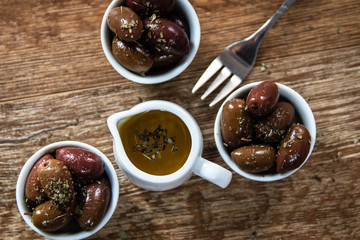 Greek Kalamata black red olives in a small white bowls with spices and small bowl with olive oil on wooden table