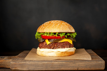 Homemade hamburger with lettuce, tomato, cheese and cucumber on a cutting board