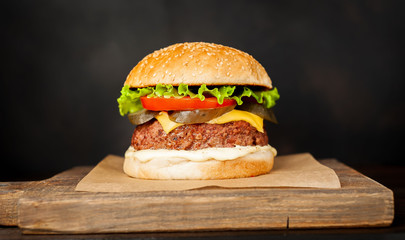 Homemade hamburger with lettuce, tomato, cheese and cucumber on a cutting board
