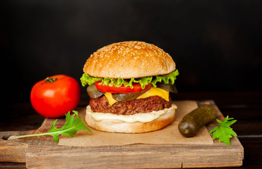 Homemade hamburger with lettuce, tomato, cheese and cucumber on a cutting board