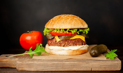 Homemade hamburger with lettuce, tomato, cheese and cucumber on a cutting board