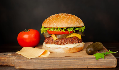 Homemade hamburger with lettuce, tomato, cheese and cucumber on a cutting board
