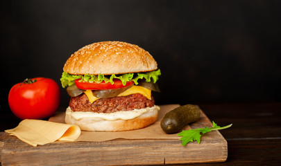Homemade hamburger with lettuce, tomato, cheese and cucumber on a cutting board