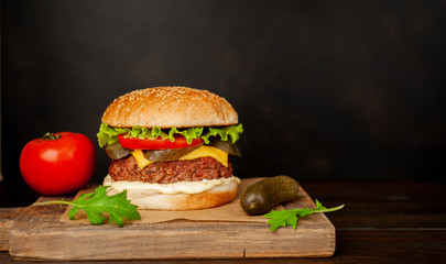 Homemade hamburger with lettuce, tomato, cheese and cucumber on a cutting board