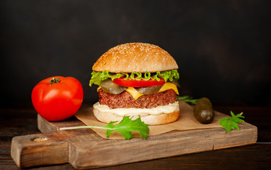 Homemade hamburger with lettuce, tomato, cheese and cucumber on a cutting board
