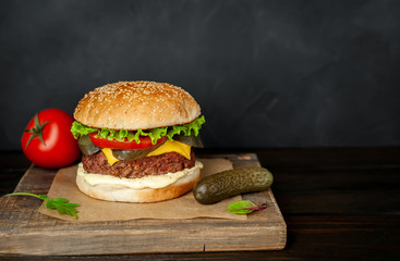 Homemade hamburger with lettuce, tomato, cheese and cucumber on a cutting board