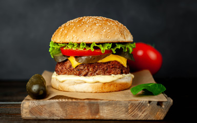 Homemade hamburger with lettuce, tomato, cheese and cucumber on a cutting board