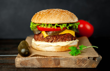 Homemade hamburger with lettuce, tomato, cheese and cucumber on a cutting board
