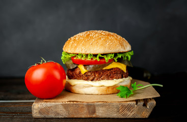 Homemade hamburger with lettuce, tomato, cheese and cucumber on a cutting board