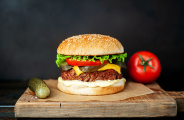 Homemade hamburger with lettuce, tomato, cheese and cucumber on a cutting board