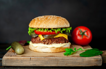 Homemade hamburger with lettuce, tomato, cheese and cucumber on a cutting board
