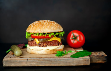 Homemade hamburger with lettuce, tomato, cheese and cucumber on a cutting board