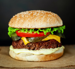 Homemade hamburger with lettuce, tomato, cheese and cucumber on a cutting board