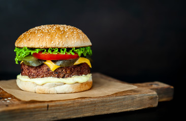Homemade hamburger with lettuce, tomato, cheese and cucumber on a cutting board